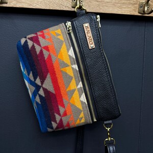 May include: A black leather crossbody bag with a colorful geometric patterned flap and a gold zipper. The bag has a brown leather tag with the text "SALATO" on it.