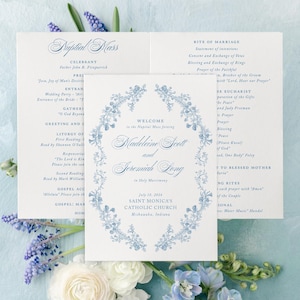 May include: Wedding invitation suite with a floral design in light blue. The invitation includes the names Madeleine Scott and Jeremiah Long, along with the date July 18, 2026, and the location Saint Monica's Catholic Church, Mishawaka, Indiana.