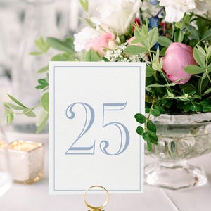May include: A white card with a blue number "25" printed on it. The card is held by a gold metal stand with a ring on top.