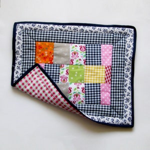 Könnte beinhalten: Eine Patchwork-Decke mit einem blauen und weißen Gingham-Rand. Die Decke besteht aus verschiedenen bunten Stoffen mit Blumen- und geometrischen Mustern. Die Decke ist in der Hälfte gefaltet und die Innenseite ist ein rosa und weißes Gingham.