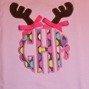 May include: A purple t-shirt with a brown reindeer applique. The reindeer has pink bows and a monogram with the letters "CHM" in a circle with a polka dot pattern.