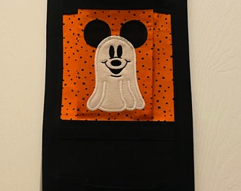 May include: A black fabric wall hanging with three pockets. Each pocket features a different Halloween-themed ghost character with Mickey Mouse ears. The top pocket has a ghost with a spiderweb and bats. The middle pocket has a ghost with a black nose and a smile. The bottom pocket has a ghost with a pink bow.