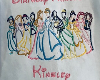 May include: White fabric embroidered with the words "Birthday Princess" and the name "Kinsley" in pink script. Below the text are embroidered images of several cartoon princesses in various colorful gowns.