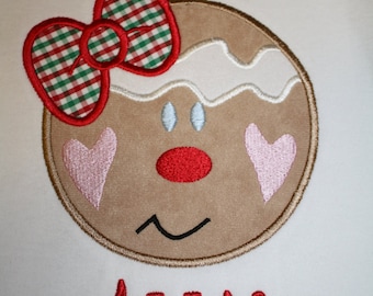 May include: White t-shirt with an embroidered gingerbread person with a red bow and the name "Annie" in red.