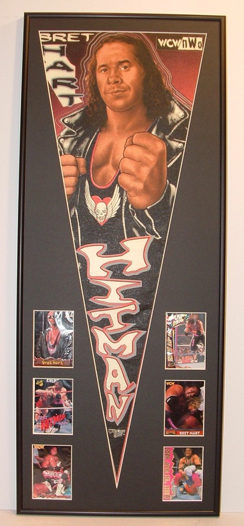 May include: Framed artwork featuring a portrait of Bret Hart, with the text "Bret Hart" and "WCW/nWo". Includes six trading cards of Bret Hart in action. The artwork is in a black frame.