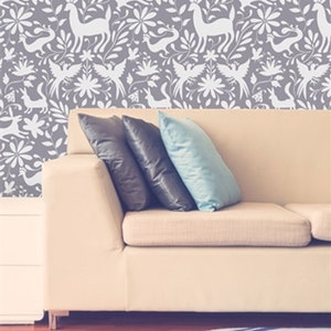 May include: A white couch with three pillows in front of a wall with a gray and white floral pattern. The couch is sitting on a wooden floor with a blue and white rug in front of it.