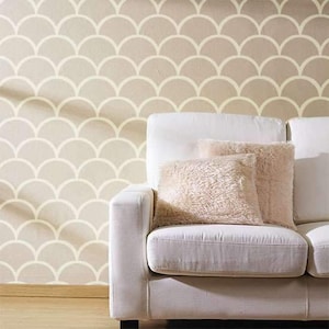 May include: A white sofa with two fluffy, light brown pillows sits in front of a wall with a repeating, cream-colored scallop pattern. The wall and pillows create a soft, neutral color palette, suitable for home decor.