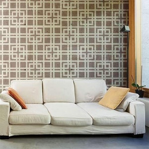 May include: A cream-colored sofa with three cushions and a matching slipcover. The sofa has two throw pillows, one orange and one yellow. The wall behind the sofa has a geometric pattern in shades of brown and white.