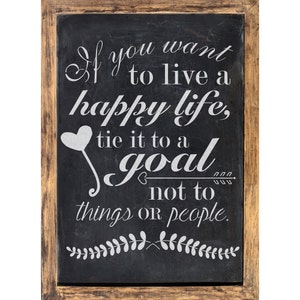 May include: A black chalkboard with a white wooden frame, featuring a motivational quote: "If you want to live a happy life, tie it to a goal not to things or people."