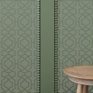 May include: A close-up of a wall with a green geometric pattern wallpaper. The wallpaper has a repeating pattern of interlocking squares and circles. The wall is accented with two vertical strips of green beadboard molding.