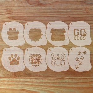 May include: Eight wooden stencils with bulldog and paw print designs. One stencil reads "GO DOGS". The stencils are light brown and are arranged on a wooden surface.