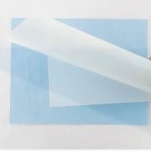 May include: A white sheet of paper is being peeled off of a light blue sheet of paper. The paper is being peeled off by a hand wearing a white glove.