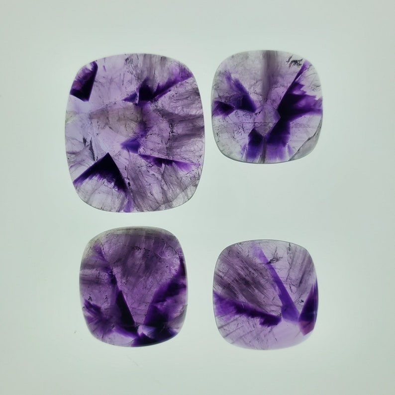May include: Four square-shaped amethyst cabochons with a purple and white color pattern. The cabochons are polished and have a smooth surface.