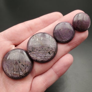 May include: Four round, purple and silver gemstone cabochons of varying sizes. The cabochons are smooth and have a striated pattern.