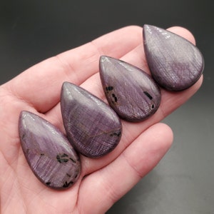 Può includere: Quattro cabochon a forma di goccia di colore viola e nero con un motivo striato.