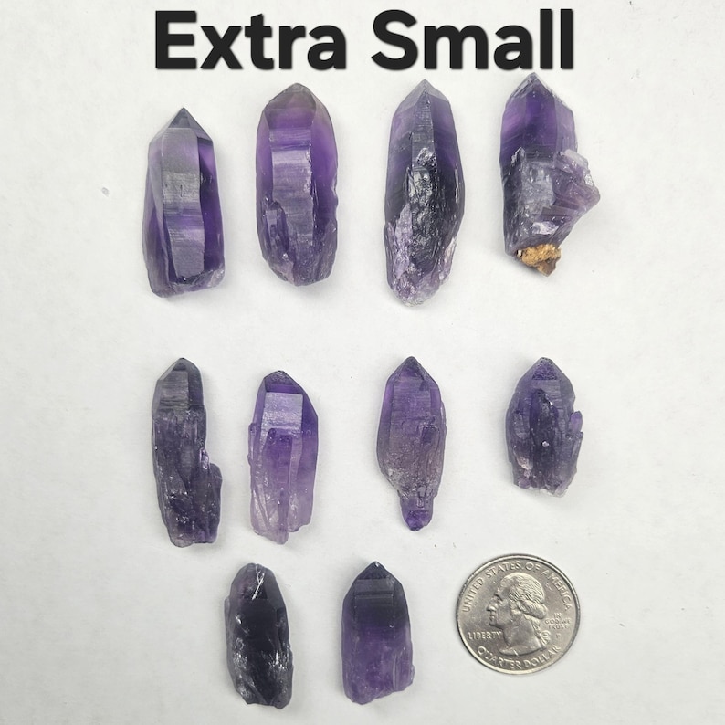 Peut inclure: Plusieurs cristaux d'am&eacute;thyste extra petits de diff&eacute;rentes formes et nuances de violet. Ils sont pr&eacute;sent&eacute;s sur une surface blanche, avec une pi&egrave;ce de monnaie pour l'&eacute;chelle. Le texte "Extra Small" est en haut.