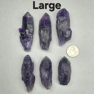 Peut inclure: Six pointes de cristal d'am&eacute;thyste de grande taille, de formes et de tailles vari&eacute;es, avec une pi&egrave;ce de monnaie pour l'&eacute;chelle. Les cristaux varient du violet fonc&eacute; au lavande clair. Le mot "Large" est imprim&eacute; en noir en haut de l'image.