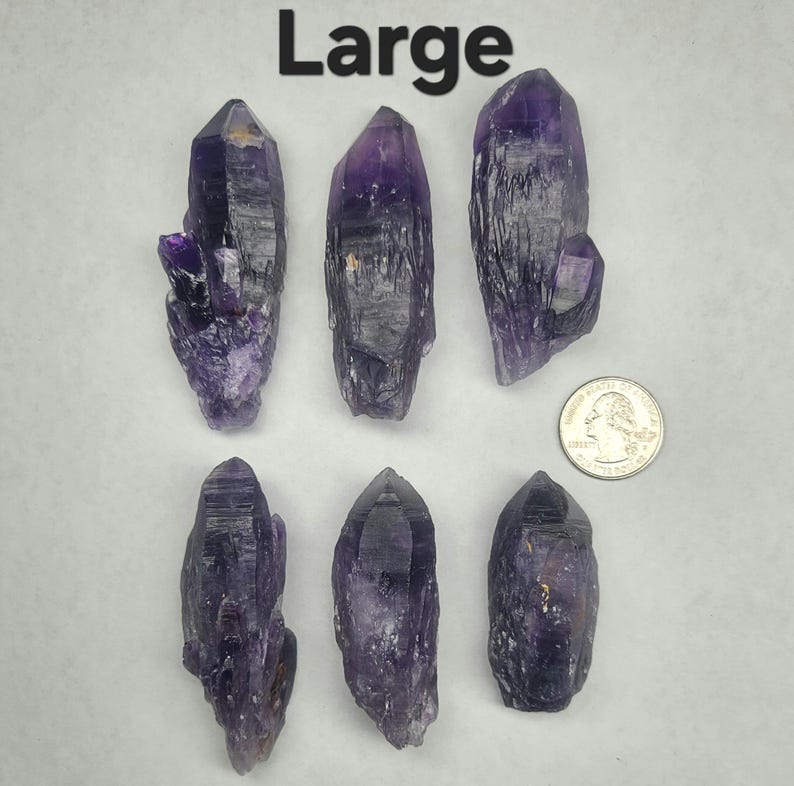 Peut inclure: Six pointes de cristal d'am&eacute;thyste de grande taille, de formes et de tailles vari&eacute;es, avec une pi&egrave;ce de monnaie pour l'&eacute;chelle. Les cristaux varient du violet fonc&eacute; au lavande clair. Le mot "Large" est imprim&eacute; en noir en haut de l'image.