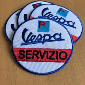 May include: Embroidered patches featuring the Vespa logo and the word "SERVIZIO" in red. The patches are circular with a white background, blue border, and a blue Vespa script. A red and blue square with a "P" is also present.