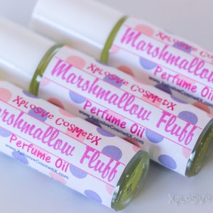May include: Close-up of three perfume oil bottles with white caps. The labels read "Marshmallow Fluff Perfume Oil" in pink text, with a polka dot design. The brand name "Xplosive CosmetiX" is also visible.