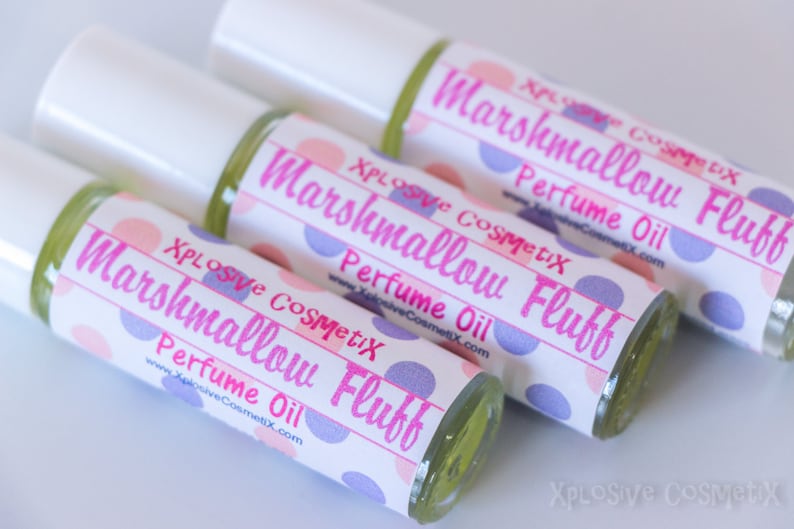 May include: Close-up of three perfume oil bottles with white caps. The labels read "Marshmallow Fluff Perfume Oil" in pink text, with a polka dot design. The brand name "Xplosive CosmetiX" is also visible.