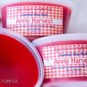 May include: Three red wax melts in clear plastic containers with white lids. Each container has a red and white checkered label that reads "XPLOSIVE COSMETIX Scented Wax Melt Apple Harvest".