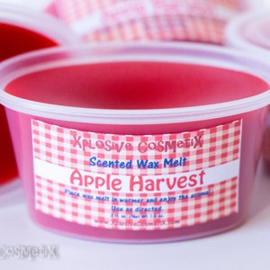 May include: A red scented wax melt in a clear plastic container with a white and red checkered label that reads "XPLOSIVE COSMETIX Scented Wax Melt Apple Harvest Place wax melt in warmer and enjoy the aroma Use as directed www.xlosivecosmetix.com"