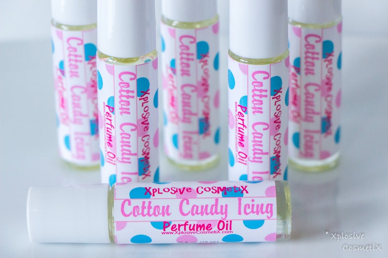 K&ouml;nnte beinhalten: Eine Sammlung von Roll-on-Parf&uuml;m&ouml;len mit der Aufschrift "Cotton Candy Icing" und rosa und blauen Tupfen. Die Flaschen sind klar, und die Etiketten enthalten den Markennamen "Xplosive Cosmetix" und die Website-Adresse.