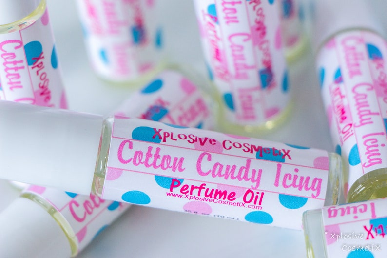 K&ouml;nnte beinhalten: Mehrere Parf&uuml;m&ouml;lflaschen mit wei&szlig;en Kappen und Etiketten. Die Etiketten zeigen "Cotton Candy Icing Perfume Oil" in Rosa und Blau, mit dem Markennamen "Xplosive Cosmetix". Die Flaschen sind mit einer klaren Fl&uuml;ssigkeit gef&uuml;llt.