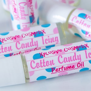 K&ouml;nnte beinhalten: Mehrere Parf&uuml;m&ouml;lflaschen mit wei&szlig;en Verschl&uuml;ssen werden gezeigt. Die Etiketten tragen die Aufschrift "Xplosive Cosmetix Cotton Candy Icing Perfume Oil" in Rosa und Blau, mit einem Tupfenmuster. Die Flaschen sind transparent und mit einer hellen Fl&uuml;ssigkeit gef&uuml;llt.