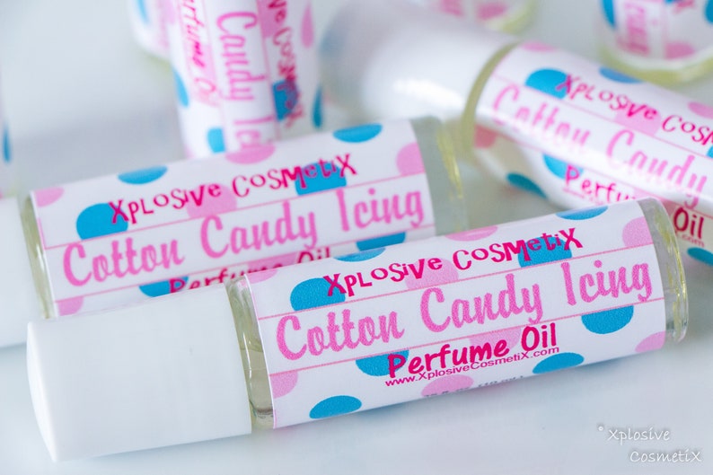 K&ouml;nnte beinhalten: Mehrere Parf&uuml;m&ouml;lflaschen mit wei&szlig;en Verschl&uuml;ssen werden gezeigt. Die Etiketten tragen die Aufschrift "Xplosive Cosmetix Cotton Candy Icing Perfume Oil" in Rosa und Blau, mit einem Tupfenmuster. Die Flaschen sind transparent und mit einer hellen Fl&uuml;ssigkeit gef&uuml;llt.