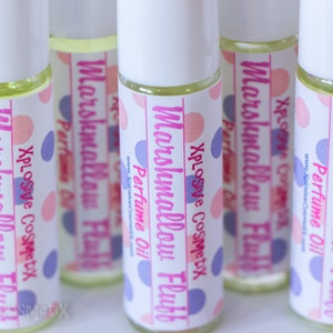May include: Several roll-on perfume bottles with white caps and labels. The labels read "Marshmallow Fluff Perfume Oil" with pink and blue polka dots. The bottles contain a light yellow liquid.