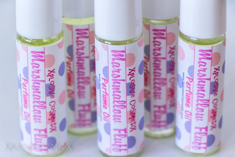 May include: Several roll-on perfume bottles with white caps and labels. The labels read "Marshmallow Fluff Perfume Oil" with pink and blue polka dots. The bottles contain a light yellow liquid.