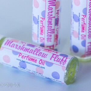 May include: Three perfume oil bottles with labels that read "Marshmallow Fluff Perfume Oil." The labels have pink and blue polka dots. The bottles are clear with a light yellow liquid inside. The website www.XplosiveCosmetiX.com is printed on the label.