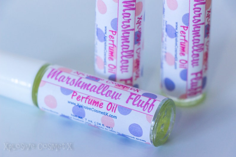May include: Three perfume oil bottles with labels that read "Marshmallow Fluff Perfume Oil." The labels have pink and blue polka dots. The bottles are clear with a light yellow liquid inside. The website www.XplosiveCosmetiX.com is printed on the label.