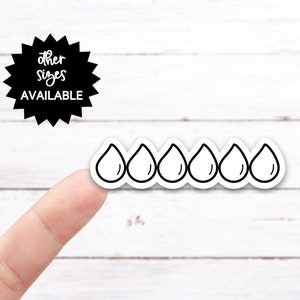 May include: A row of six black and white water drop stickers on a white wooden background.