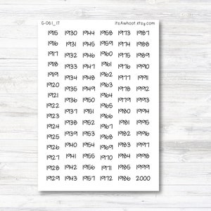 May include: A white sticker sheet with black handwritten numbers from 1915 to 2000. The numbers are arranged in columns and rows. The text "itsAwhoot.etsy.com" is in the upper right corner. The sticker sheet is on a light wood grain surface.