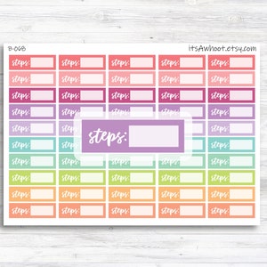May include: A sheet of colorful planner stickers with the word "steps" written on them. The stickers are in various shades of pink, purple, blue, green, and yellow. Each sticker has a blank space for writing.