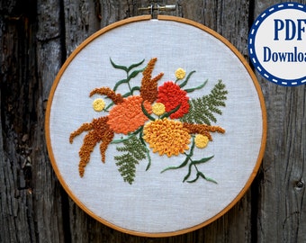May include: Embroidered hoop art featuring a floral design with orange, yellow, and brown flowers and green leaves. The hoop is made of wood and has a white fabric background.