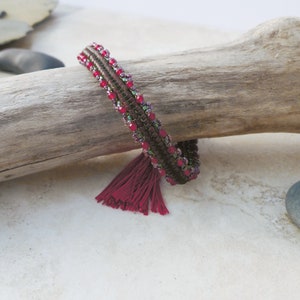 May include: A beaded bracelet with a maroon tassel. The bracelet is made with brown and iridescent beads and has a maroon tassel.
