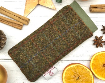 May include: A green, brown, and blue tweed phone case with a small label that says "Harris Tweed." The case is lying on a white surface with various decorative items around it.