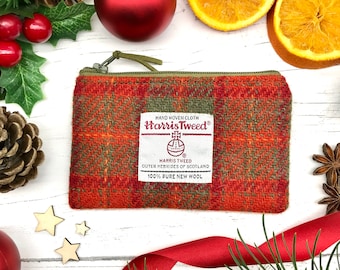 Könnte beinhalten: Eine kleine orangefarbene und grüne Tweed-Münzbörse mit Reißverschluss. Die Börse hat ein Etikett mit der Aufschrift "HAND WOVEN CLOTH Harris Tweed® HARRIS TWEED OUTER HEBRIDES OF SCOTLAND 100% PURE NEW WOOL".