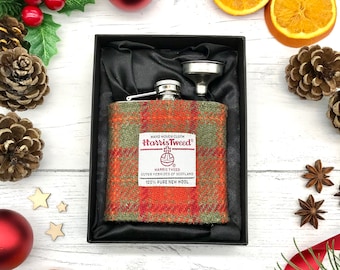 May include: A stainless steel hip flask with a green, orange, and red Harris Tweed fabric cover. The flask is in a black box with a funnel. The fabric cover has the text "HAND WOVEN CLOTH Harris Tweed HARRIS TWEED OUTER HEBRIDES OF SCOTLAND 100% PURE NEW WOOL".