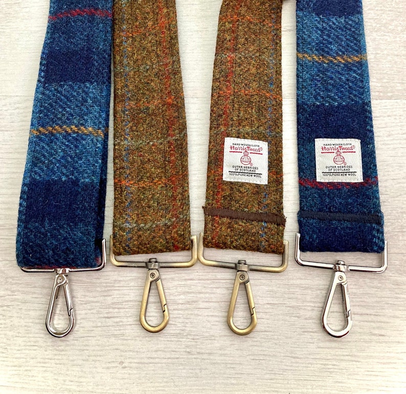 Puede incluir: Tres correas de c&aacute;mara de tweed con cierres met&aacute;licos. Las correas son de patrones de cuadros azules y marrones. Las correas tienen una etiqueta que dice "Harris Tweed" con las palabras "Hand Woven" y "Outer Hebrides of Scotland" impresas debajo.
