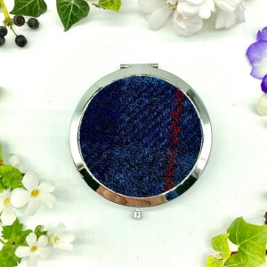 Può includere: Uno specchio compatto rotondo in argento con un design in feltro blu e rosso. Lo specchio è chiuso e il design in feltro è visibile.