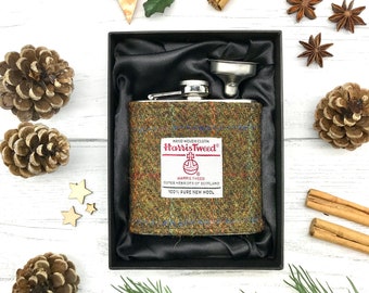 May include: A stainless steel hip flask with a Harris Tweed fabric cover. The flask is in a black velvet box with a funnel. The fabric cover has the Harris Tweed logo and the words "Hand Woven Cloth" and "100% Pure New Wool".