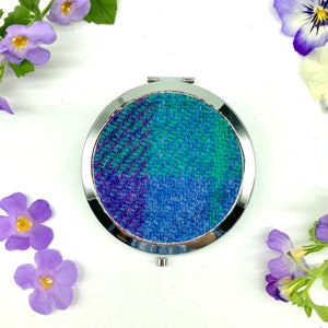 Può includere: Uno specchio compatto rotondo in argento con un design in tessuto a quadri blu, verde e viola.
