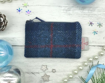 May include: A small blue and red plaid zippered pouch with a "House of Tweed" label. The pouch is on a white wooden surface with blue and silver ornaments and white pearl beads.