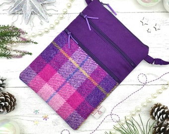 May include: A purple crossbody bag with a pink and purple plaid pattern on the front flap. The bag has two zippered compartments and a long strap.
