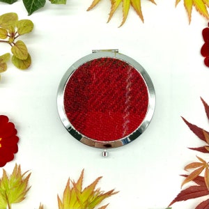 Può includere: Uno specchio compatto rotondo in argento con un design in tessuto rosso a quadri sul coperchio.